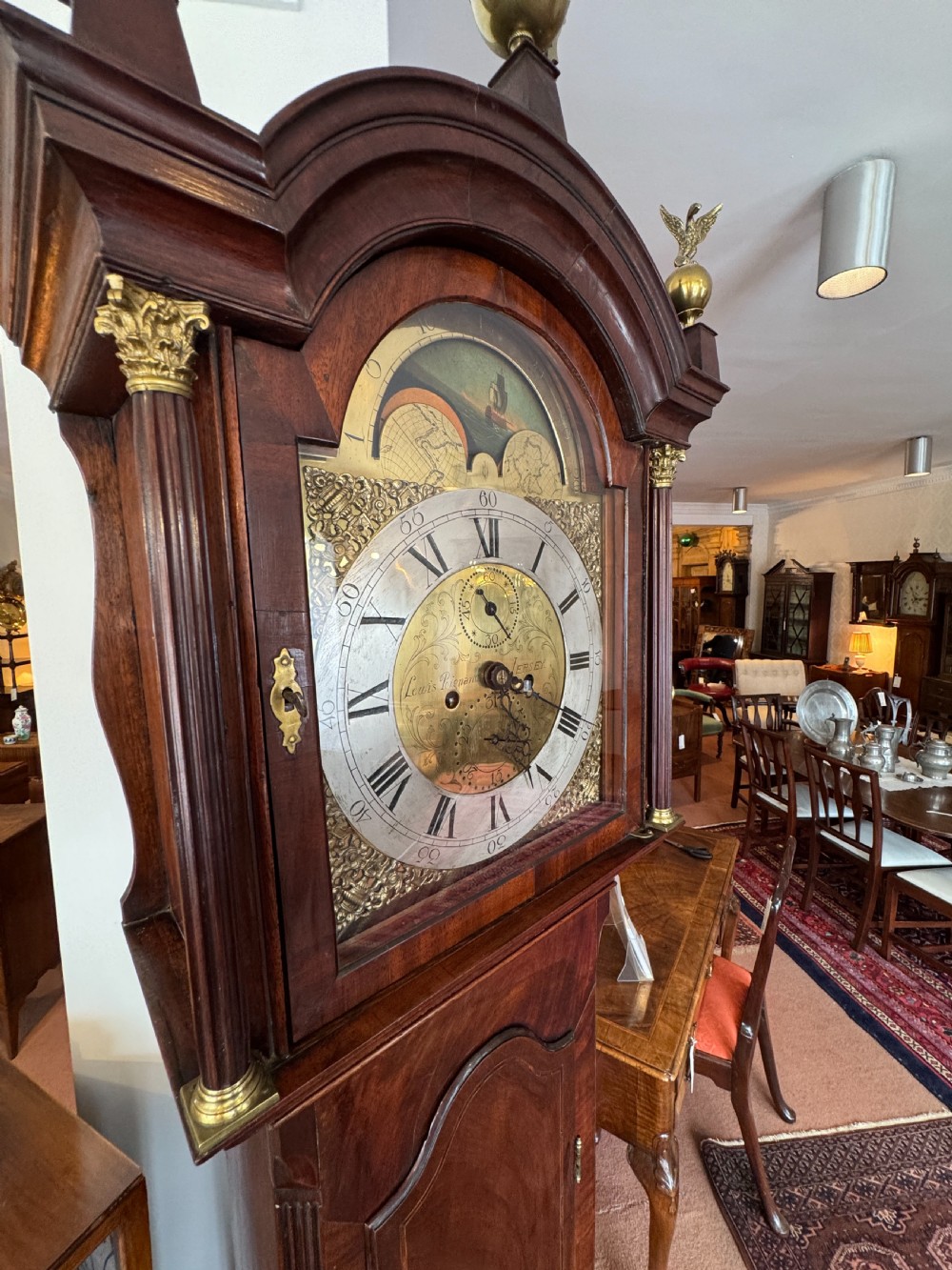 A tall Georgian mahogany longcase clock featuring a swan-neck pediment hood topped with three brass eagle finials and an ornate brass dial. View VI