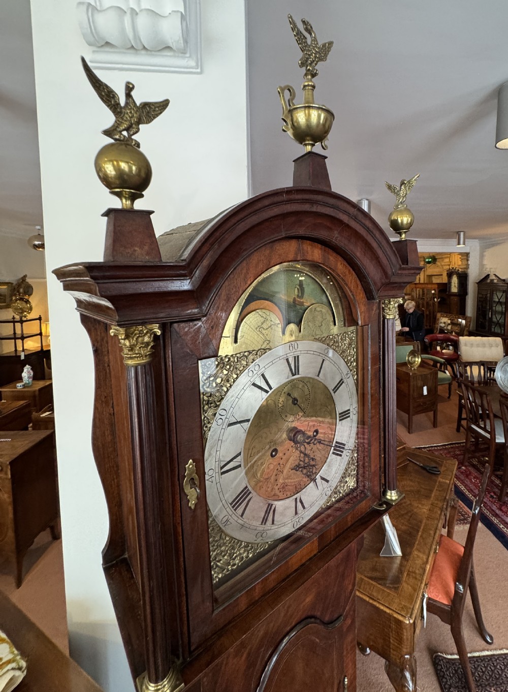 A tall Georgian mahogany longcase clock featuring a swan-neck pediment hood topped with three brass eagle finials and an ornate brass dial. View VII