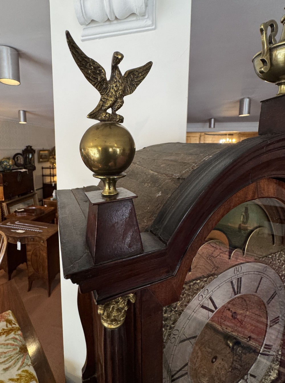 A tall Georgian mahogany longcase clock featuring a swan-neck pediment hood topped with three brass eagle finials and an ornate brass dial. View IX