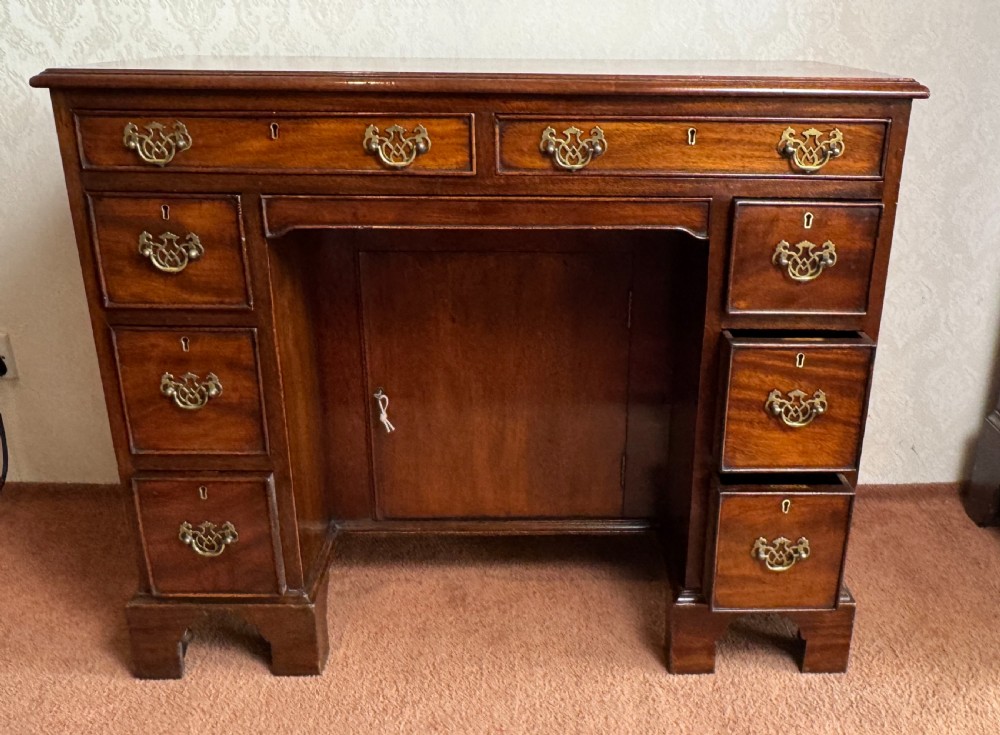 An 18th-century Georgian mahogany kneehole dressing table featuring multiple drawers with brass handles, a central recessed cupboard, and bracket feet.
