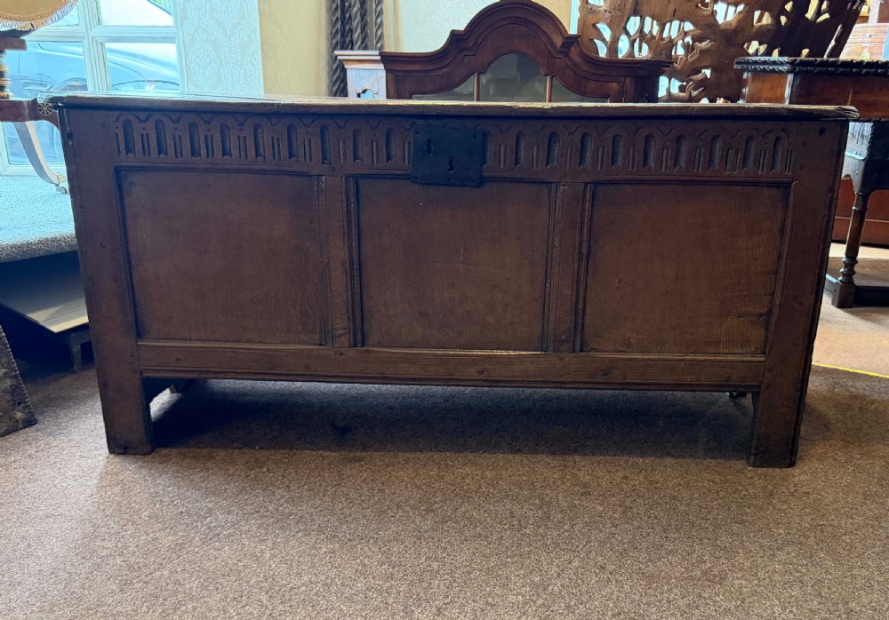 A late 17th-century English oak coffer featuring a three-panel front, a carved upper frieze, a hinged plank top, and a central iron lock plate. View III