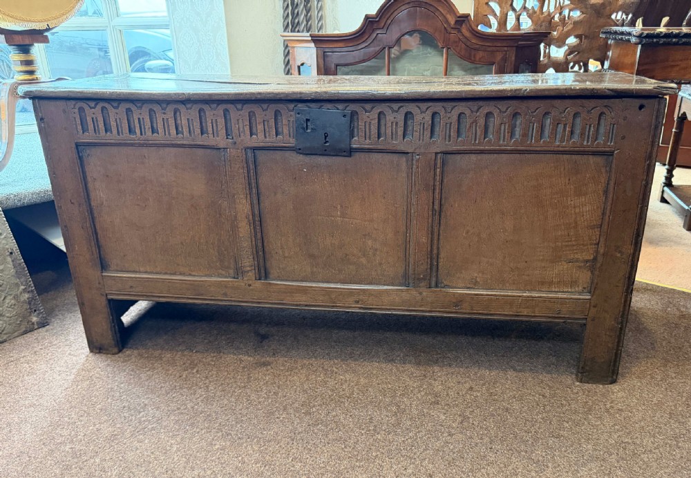 A late 17th-century English oak coffer featuring a three-panel front, a carved upper frieze, a hinged plank top, and a central iron lock plate. View IV