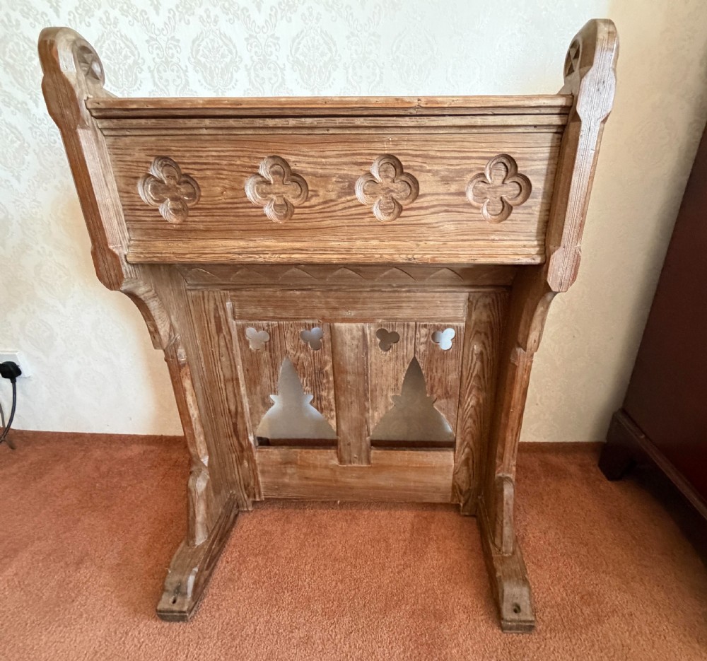 A solid pine Gothic Revival church lectern featuring carved trefoil and lancet arch cutouts, a sloped reading surface, and an open lower shelf. View VII