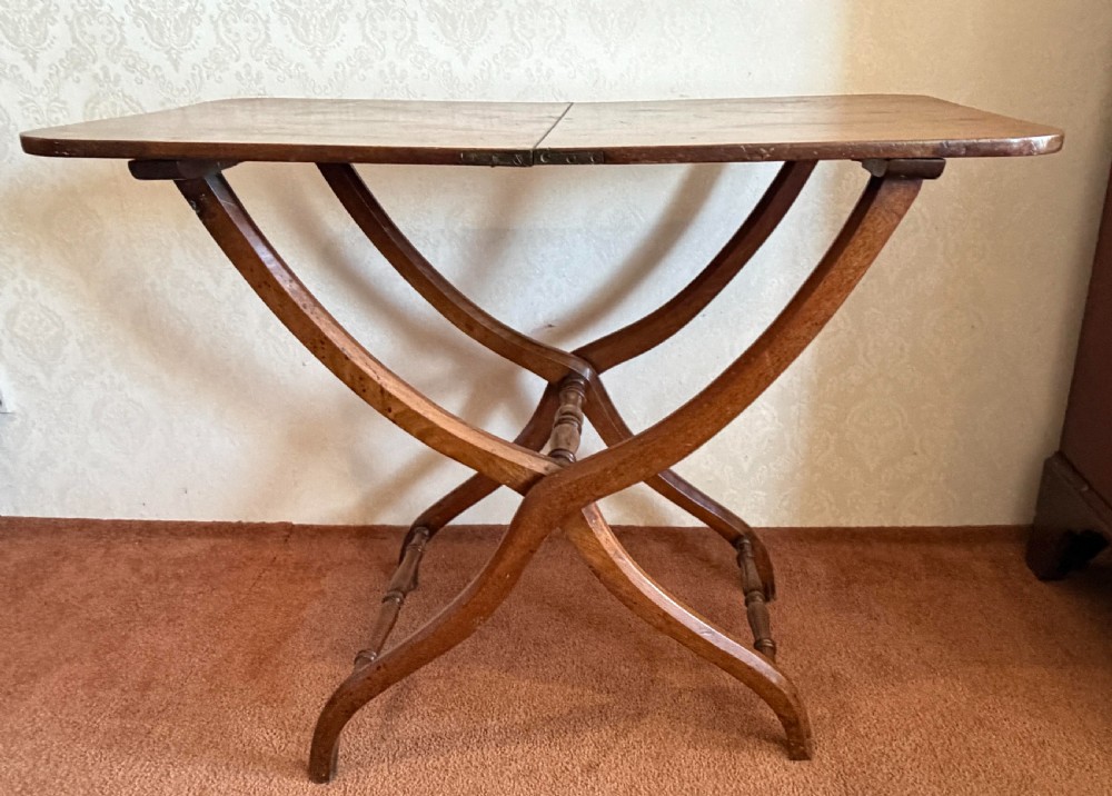 A warm brown wooden antique coaching table featuring a hinged rectangular top supported by curved X-frame legs and turned stretchers.