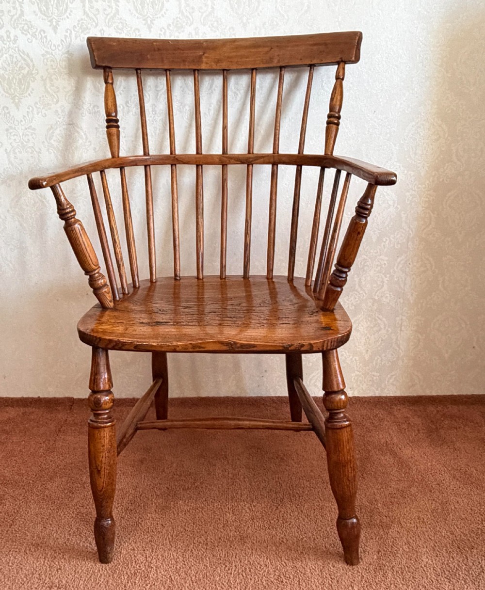 An 18th-century comb-back Windsor armchair made of polished timber with turned legs, a shaped seat, and vertical back spindles.