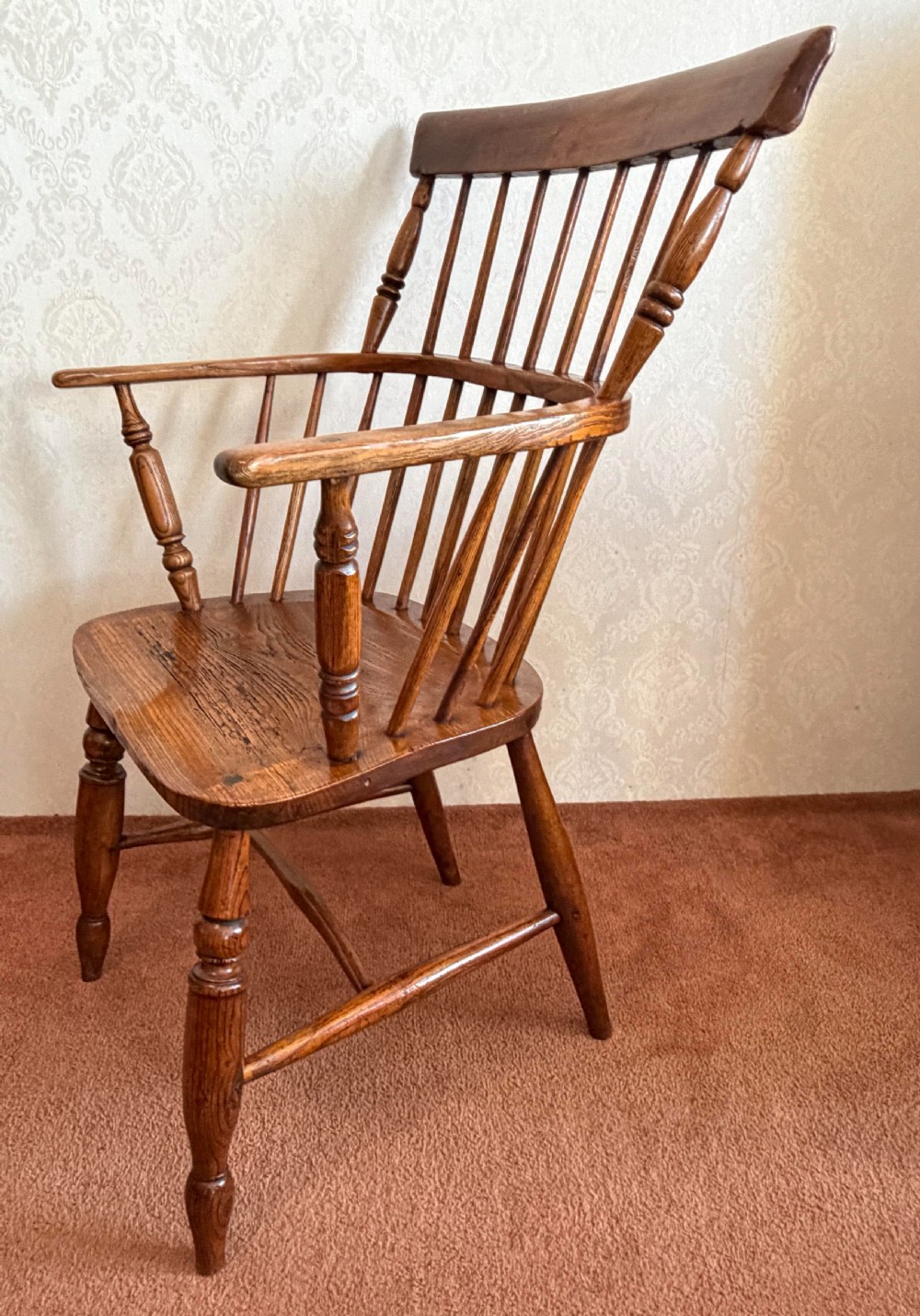 An 18th-century comb-back Windsor armchair made of polished timber with turned legs, a shaped seat, and vertical back spindles. View III