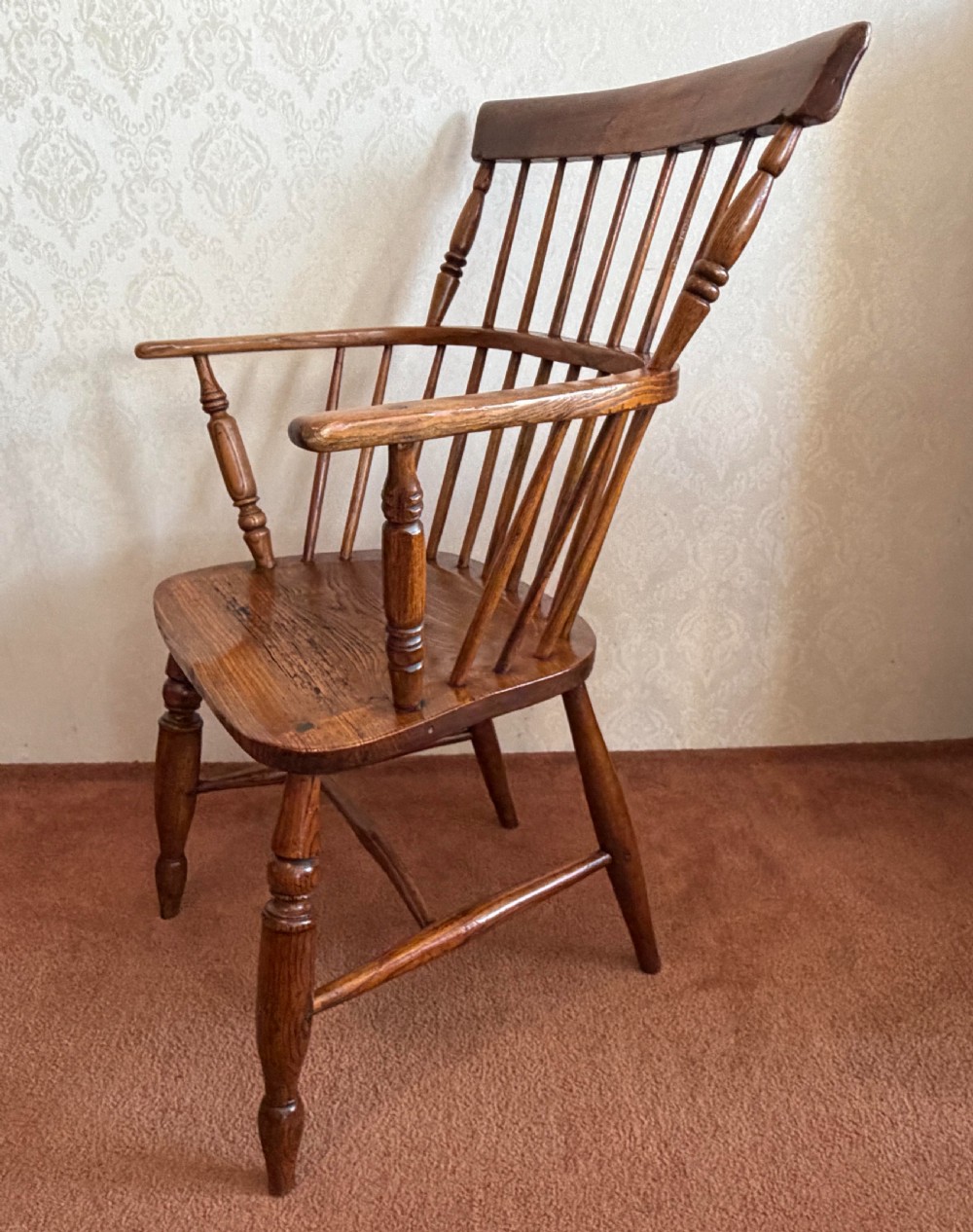 An 18th-century comb-back Windsor armchair made of polished timber with turned legs, a shaped seat, and vertical back spindles. View IV