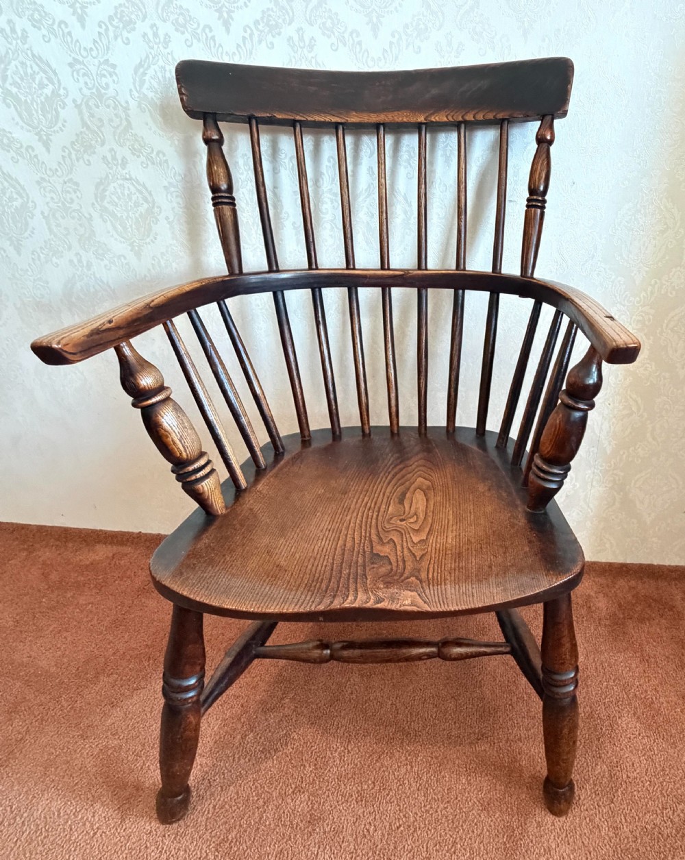 An 18th-century dark ash Windsor armchair featuring a comb-back crest rail, spindle back, shaped saddle seat, turned legs, and stretchers.