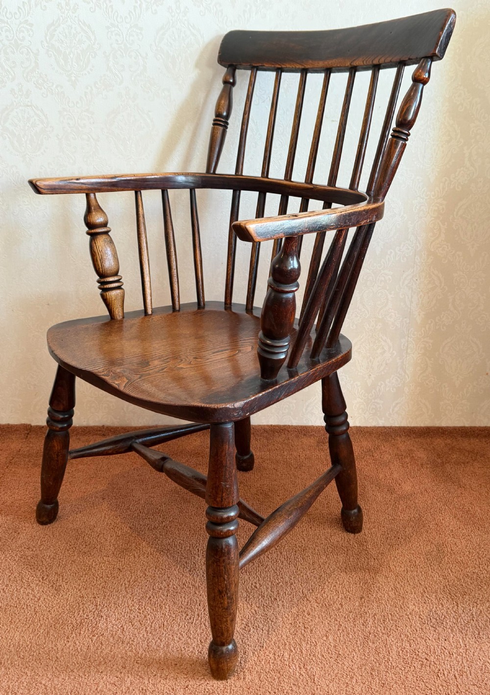 An 18th-century dark ash Windsor armchair featuring a comb-back crest rail, spindle back, shaped saddle seat, turned legs, and stretchers. View II