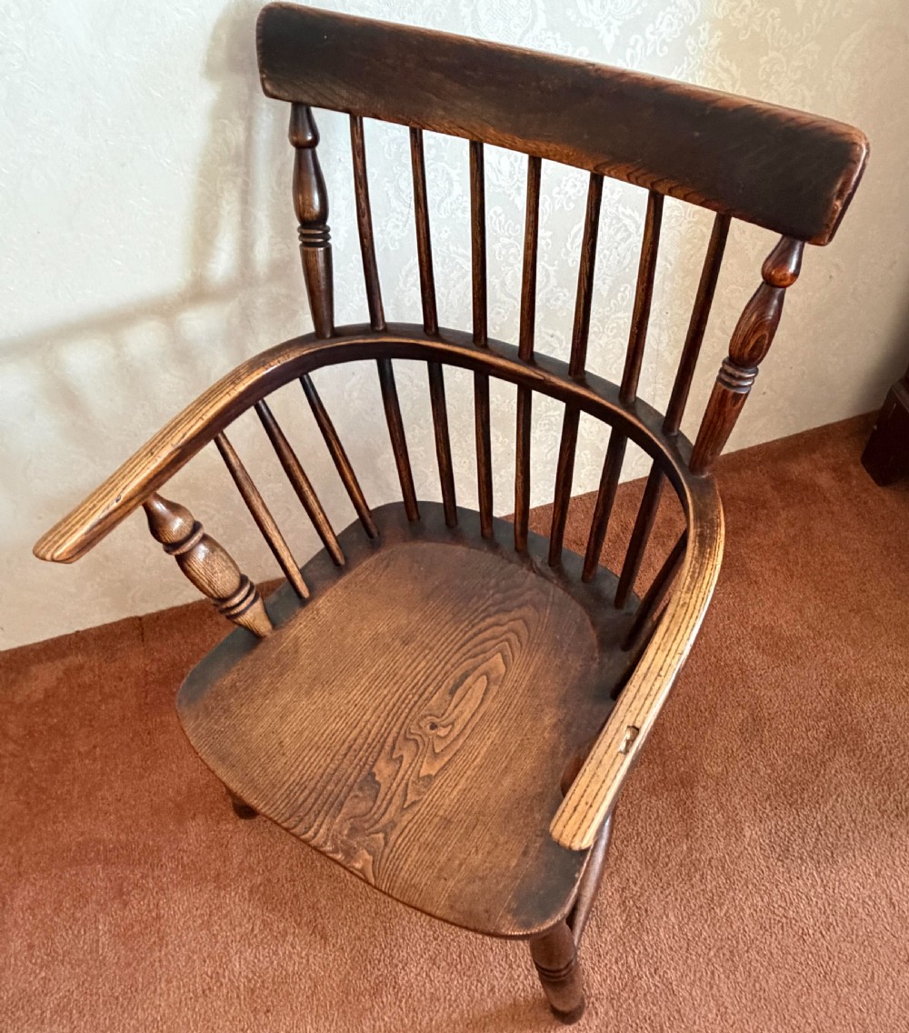 An 18th-century dark ash Windsor armchair featuring a comb-back crest rail, spindle back, shaped saddle seat, turned legs, and stretchers. View III
