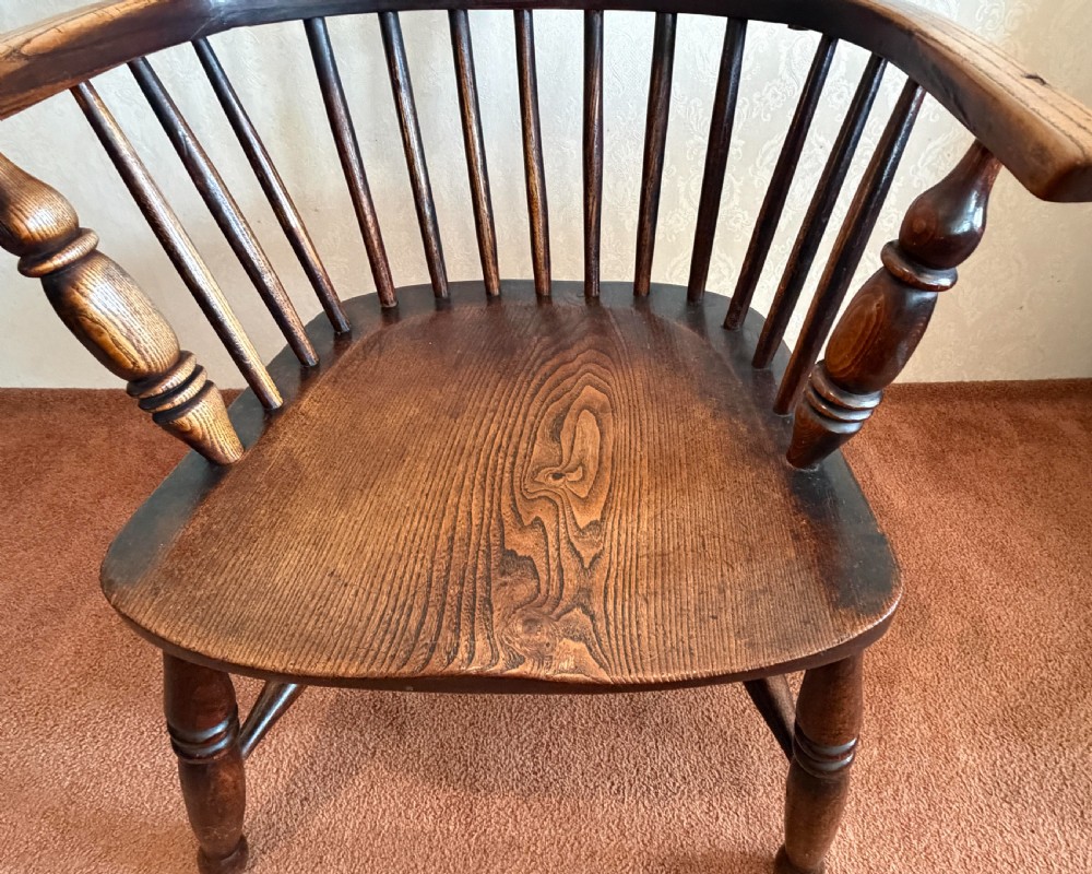 An 18th-century dark ash Windsor armchair featuring a comb-back crest rail, spindle back, shaped saddle seat, turned legs, and stretchers. View IV