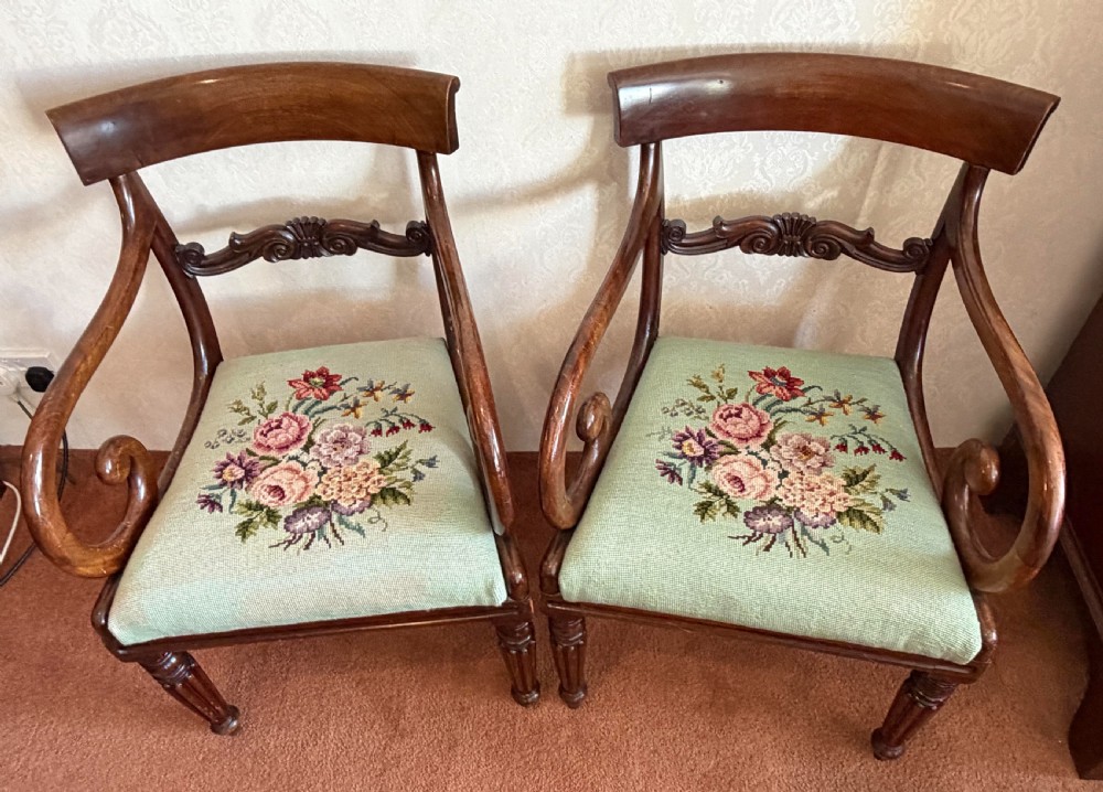 A pair of antique mahogany carver armchairs featuring swept scroll arms, carved central rails, turned fluted front legs, and green needlepoint floral upholstered seats. View II