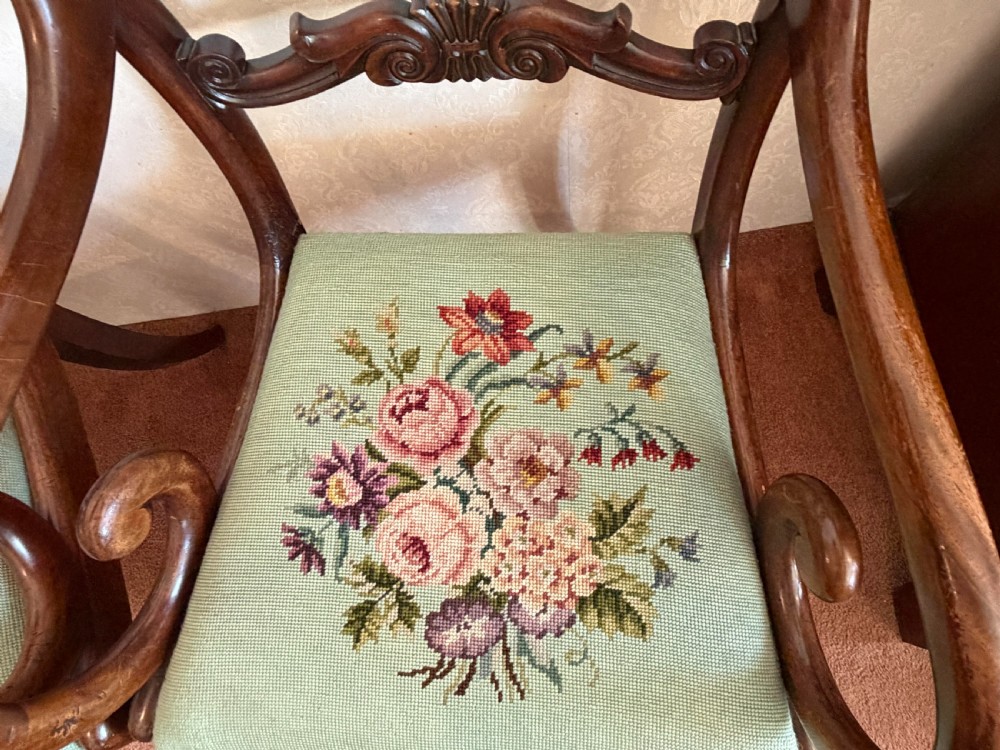 A pair of antique mahogany carver armchairs featuring swept scroll arms, carved central rails, turned fluted front legs, and green needlepoint floral upholstered seats. View III
