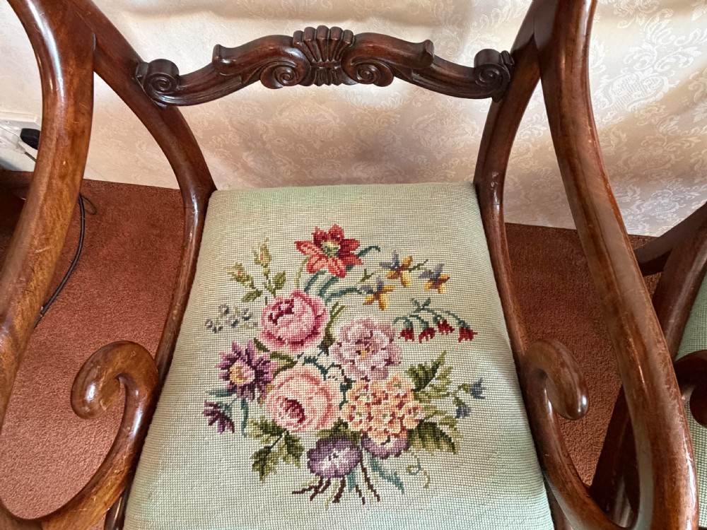 A pair of antique mahogany carver armchairs featuring swept scroll arms, carved central rails, turned fluted front legs, and green needlepoint floral upholstered seats. View IV