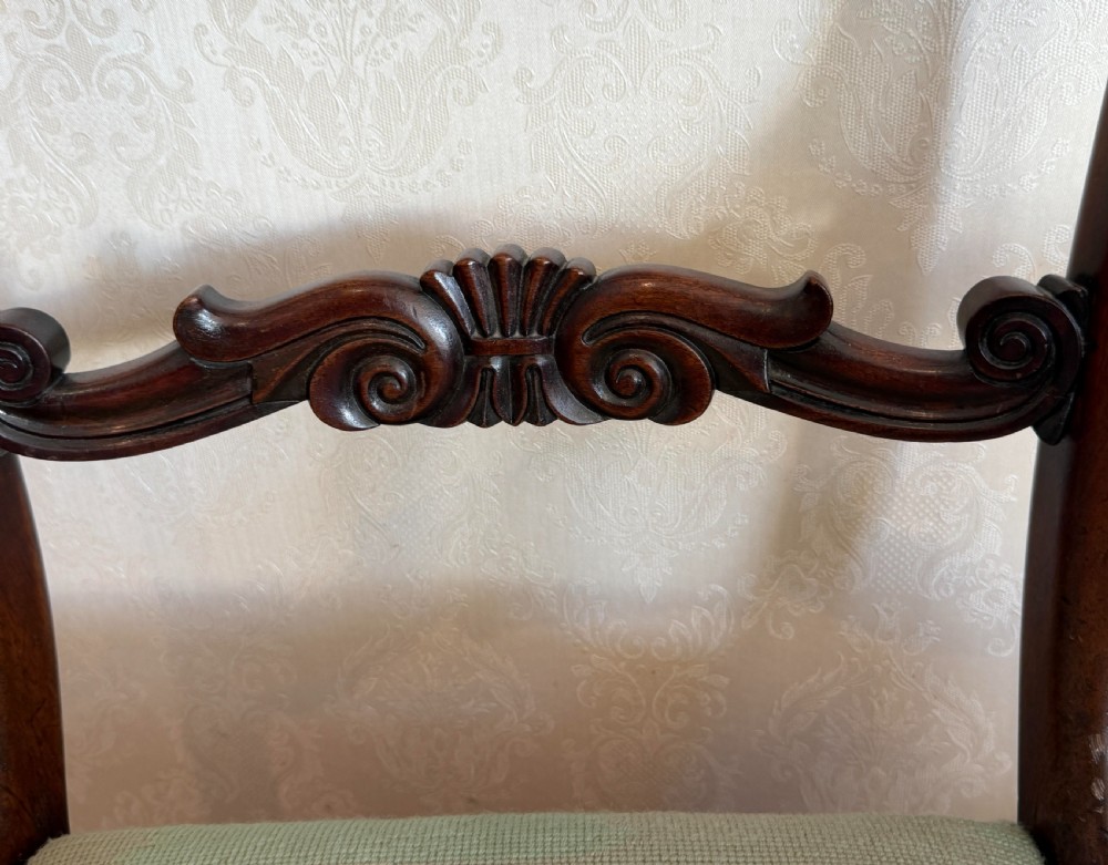 A pair of antique mahogany carver armchairs featuring swept scroll arms, carved central rails, turned fluted front legs, and green needlepoint floral upholstered seats. View V