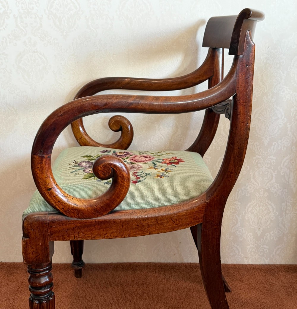 A pair of antique mahogany carver armchairs featuring swept scroll arms, carved central rails, turned fluted front legs, and green needlepoint floral upholstered seats. View VI