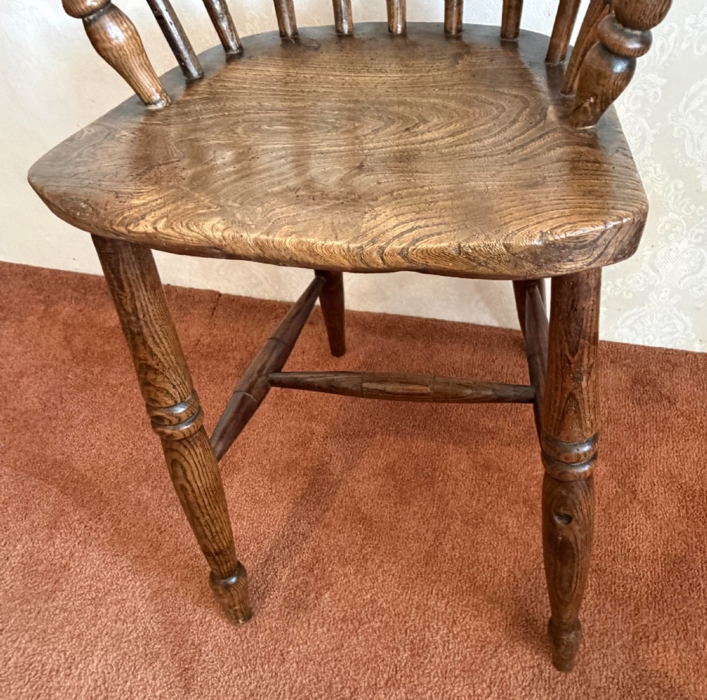 A dark wood antique childs Windsor high chair featuring a steam-bent hoop back, vertical spindles, shaped armrests, and turned legs. View II