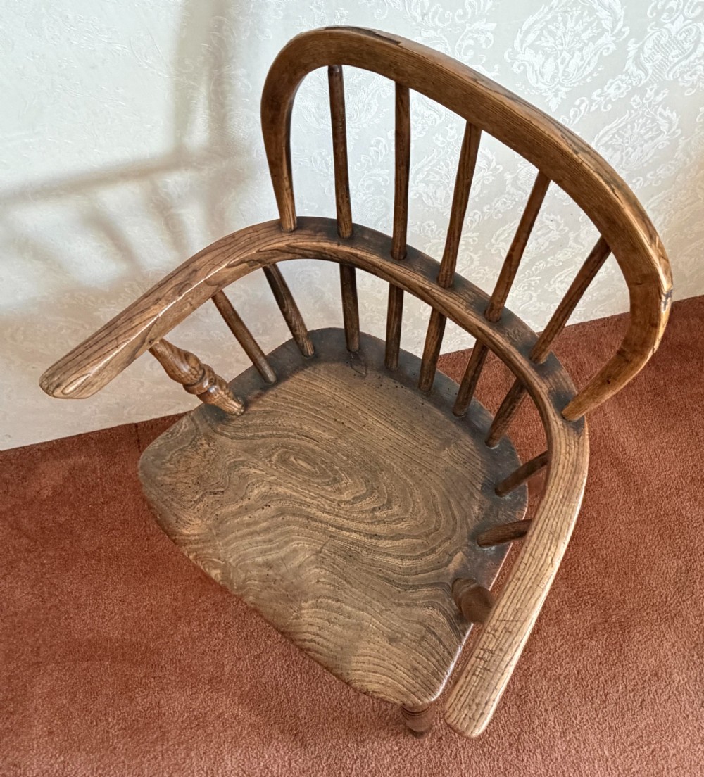 A dark wood antique childs Windsor high chair featuring a steam-bent hoop back, vertical spindles, shaped armrests, and turned legs. View IV