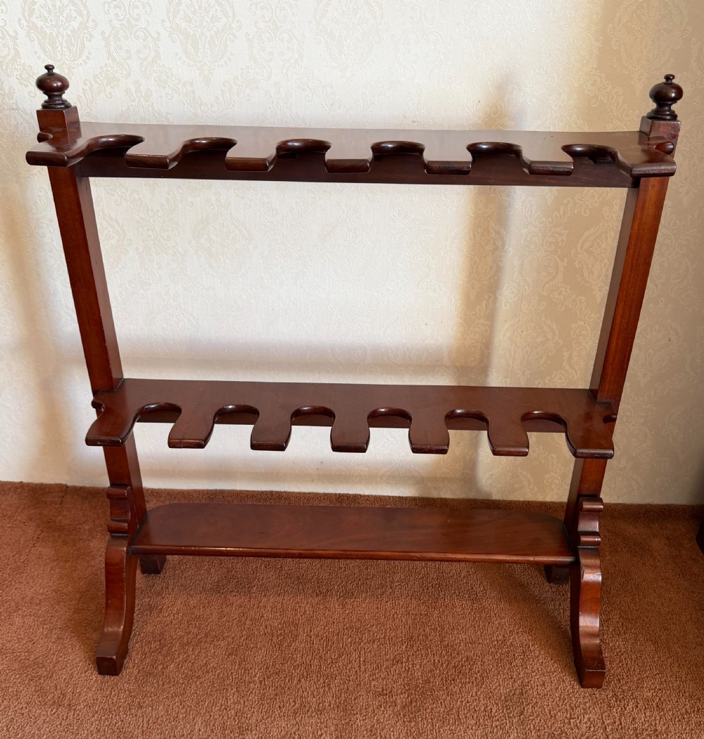 A mahogany wooden boot and whip stand featuring two notched horizontal tiers, top finials, and a lower shelf on curved feet.