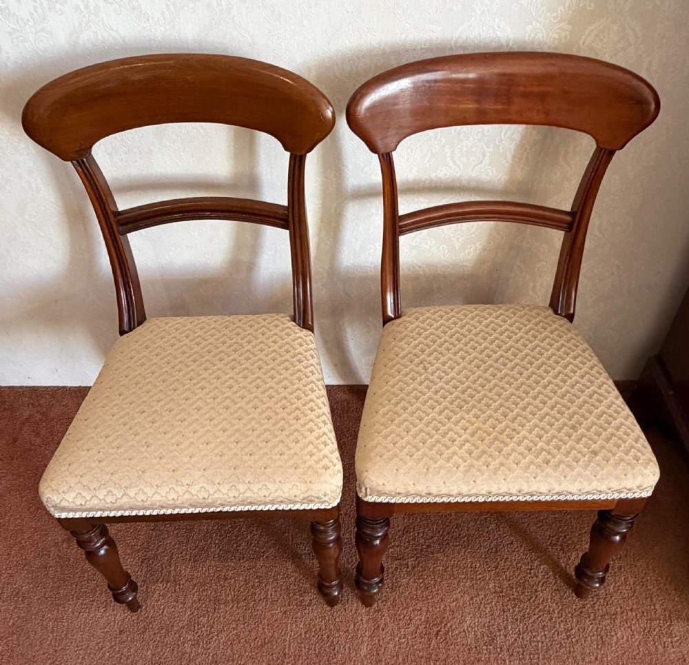 A mahogany dining chair featuring a curved top rail, horizontal bar back, turned front legs, and a beige patterned upholstered seat. View V