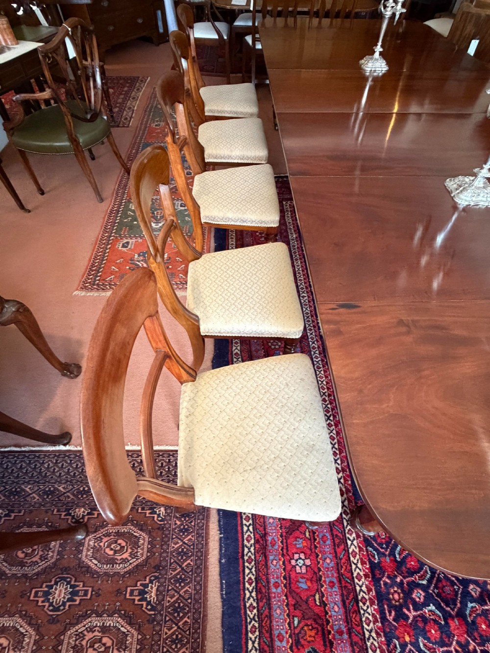 A mahogany dining chair featuring a curved top rail, horizontal bar back, turned front legs, and a beige patterned upholstered seat. View X