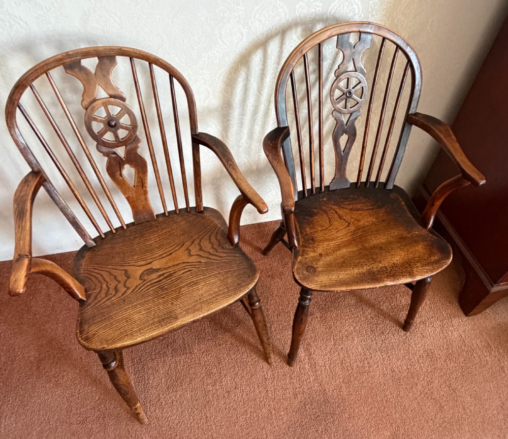 A near pair of wooden wheelback Windsor armchairs with curved hoops, turned legs, and carved central back splats.