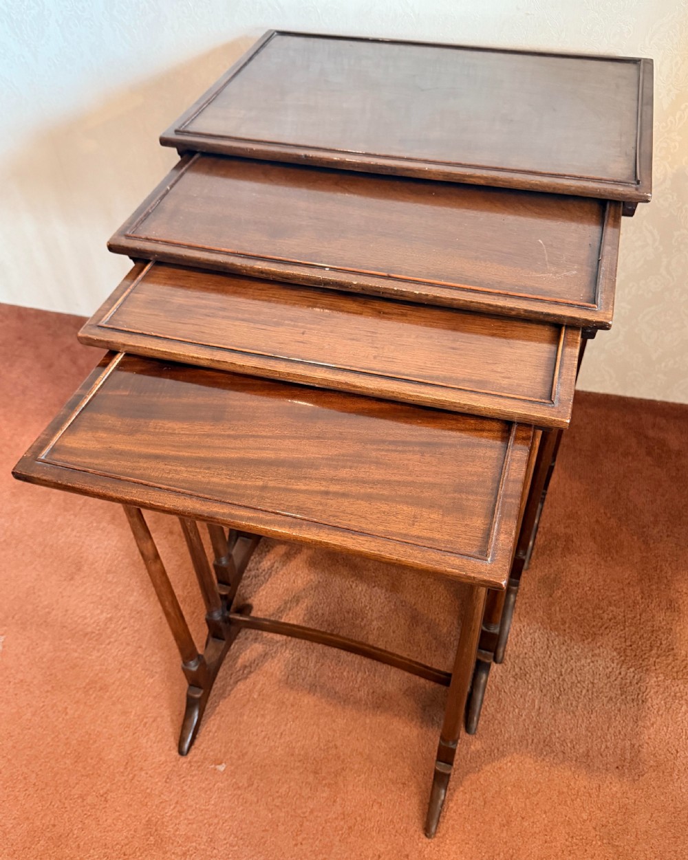A set of four graduated mahogany nesting tables featuring raised rim borders and slender turned legs stacked together.