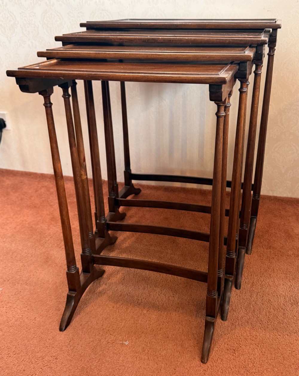 A set of four graduated mahogany nesting tables featuring raised rim borders and slender turned legs stacked together. View II