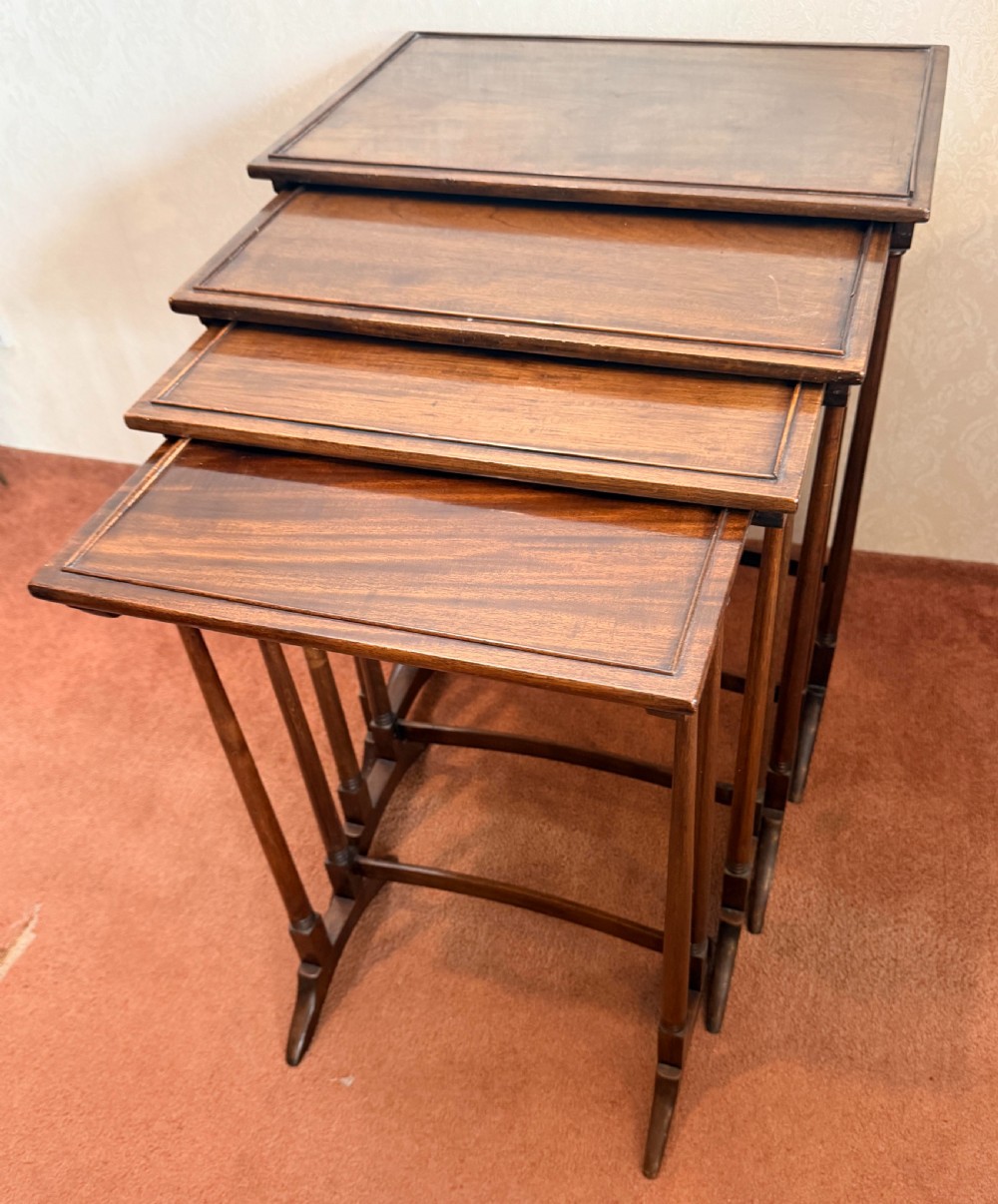 A set of four graduated mahogany nesting tables featuring raised rim borders and slender turned legs stacked together. View III