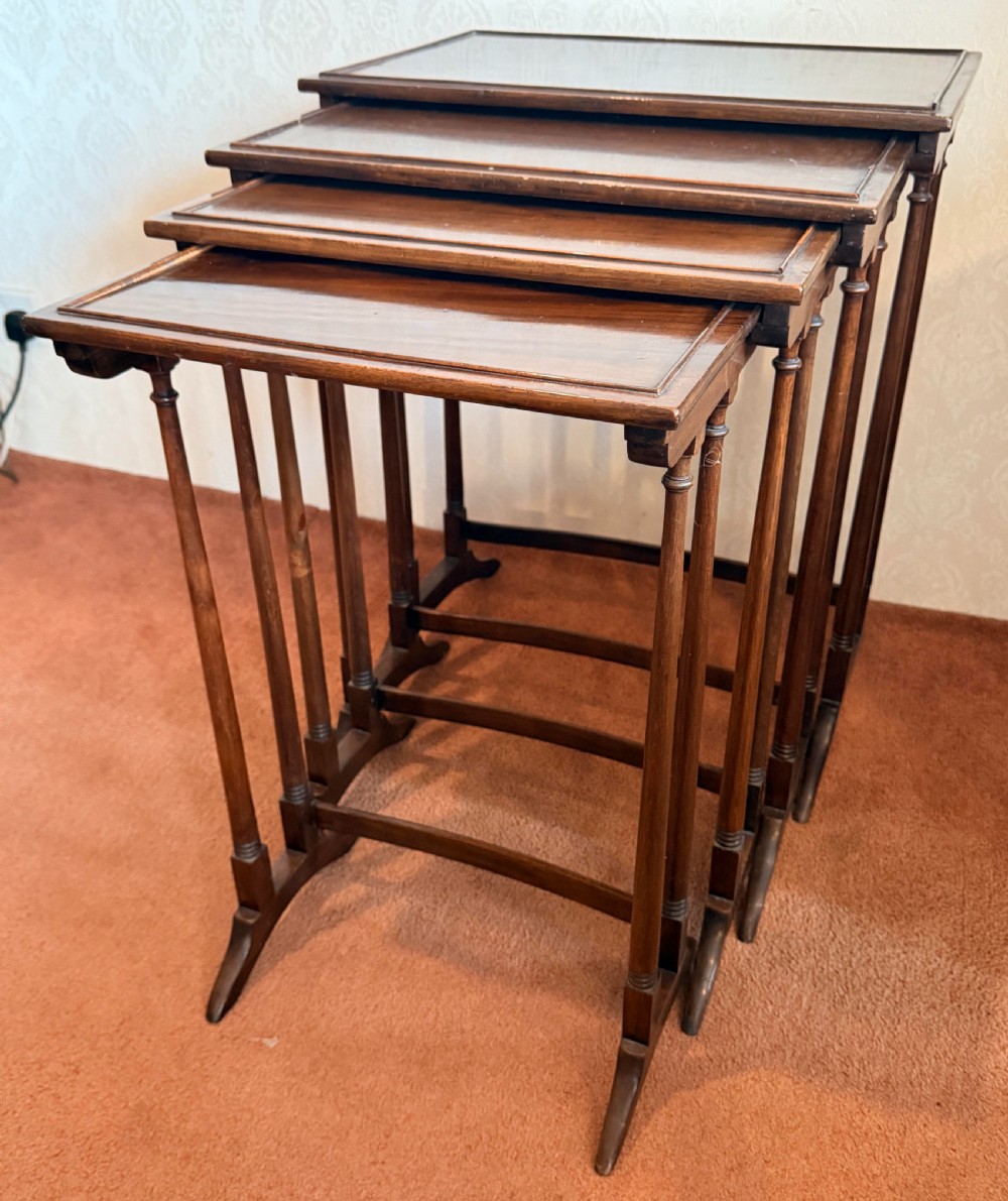 A set of four graduated mahogany nesting tables featuring raised rim borders and slender turned legs stacked together. View V