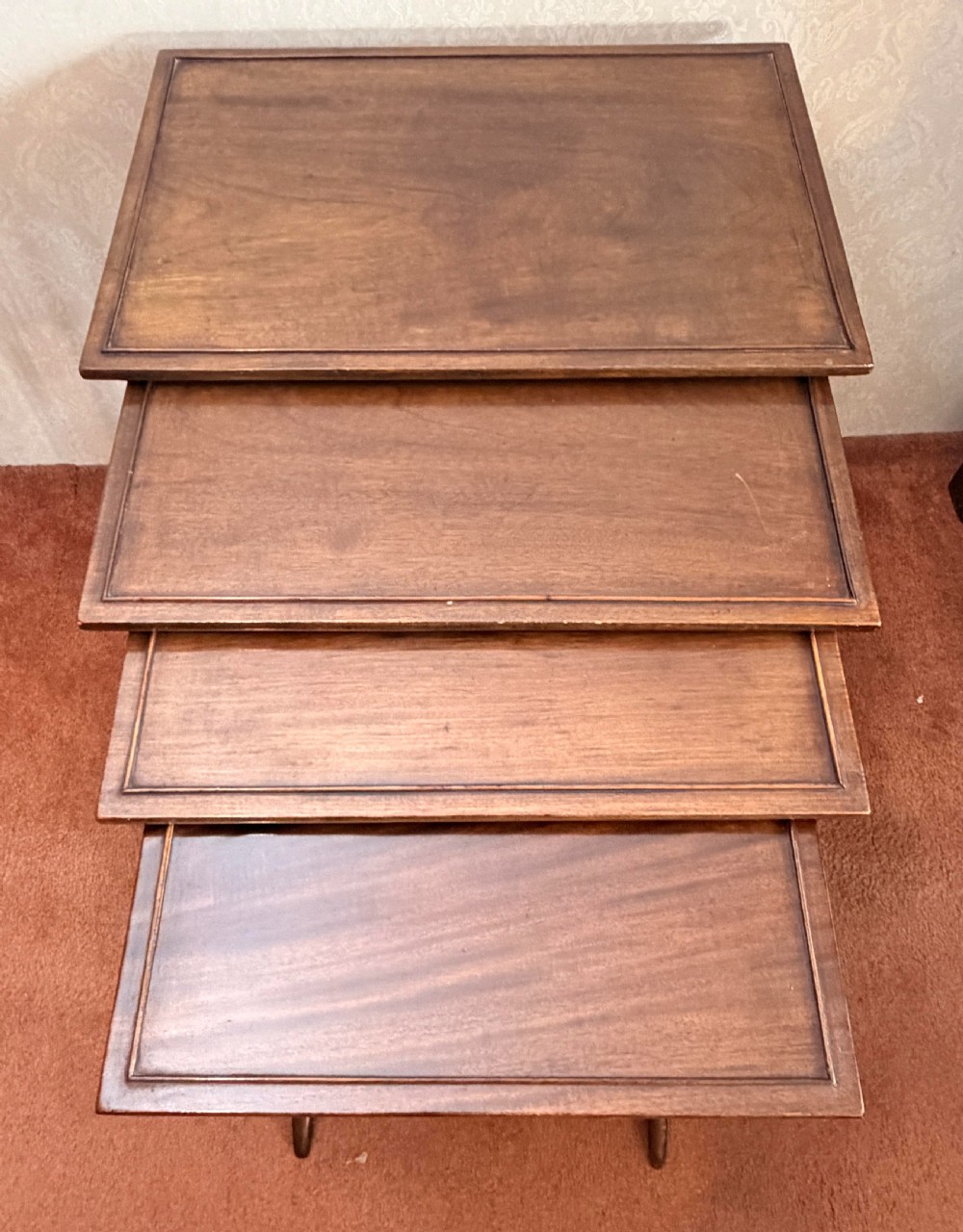 A set of four graduated mahogany nesting tables featuring raised rim borders and slender turned legs stacked together. View VI
