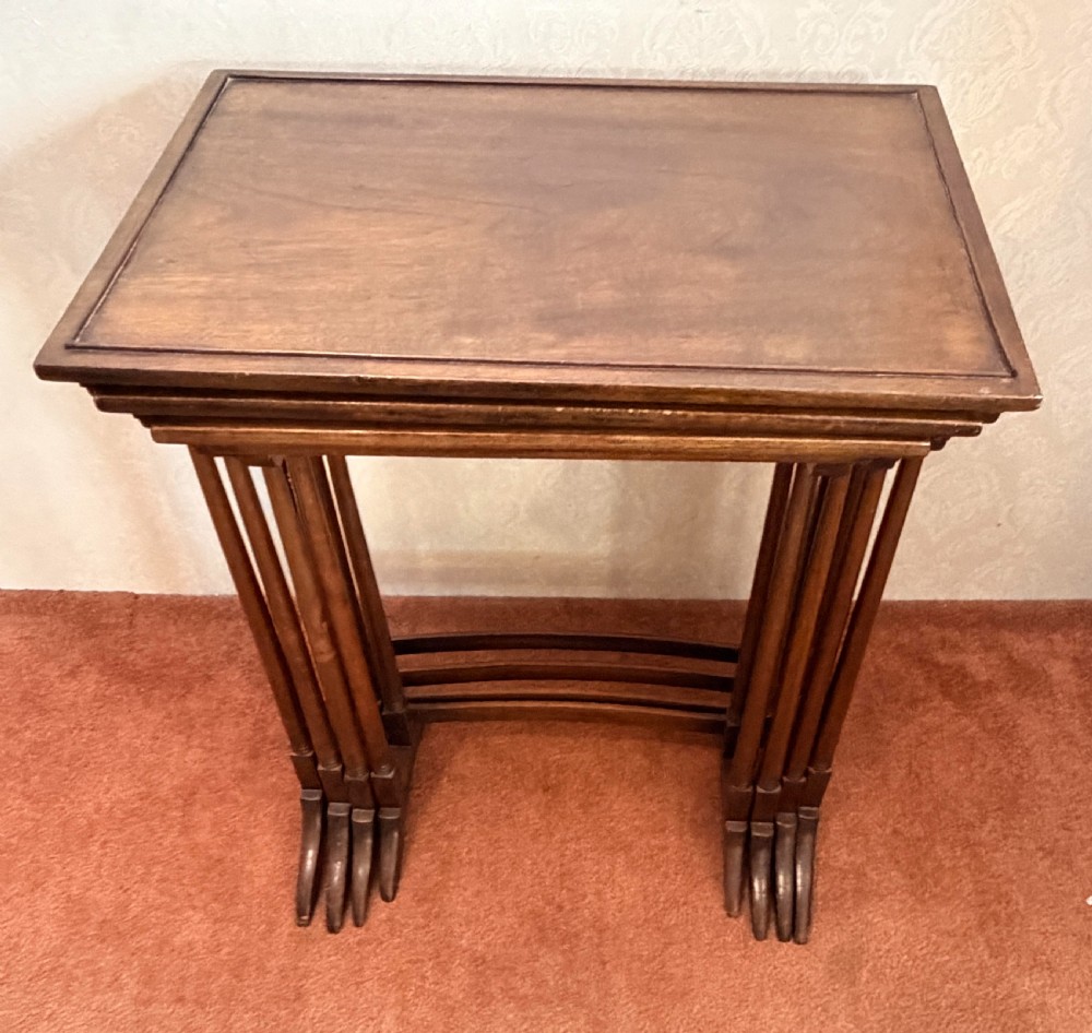 A set of four graduated mahogany nesting tables featuring raised rim borders and slender turned legs stacked together. View VII
