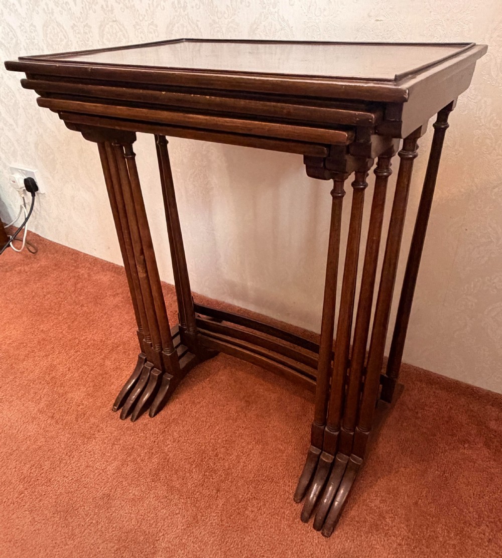 A set of four graduated mahogany nesting tables featuring raised rim borders and slender turned legs stacked together. View VIII