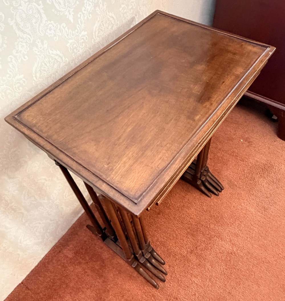 A set of four graduated mahogany nesting tables featuring raised rim borders and slender turned legs stacked together. View IX