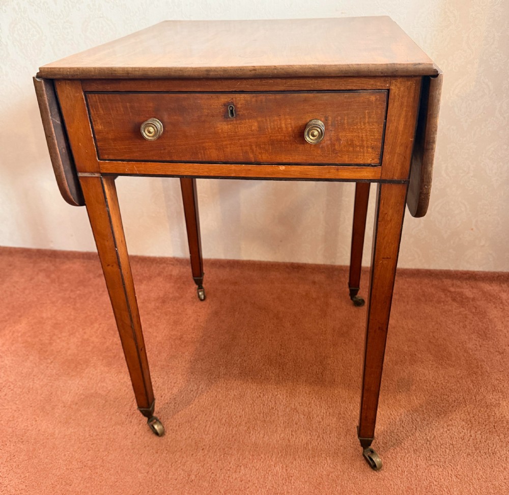A Georgian mahogany Pembroke side table featuring two hinged drop leaves, a single drawer with brass knobs, string-inlaid square tapered legs, and brass castors.