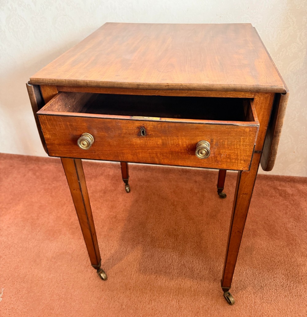 A Georgian mahogany Pembroke side table featuring two hinged drop leaves, a single drawer with brass knobs, string-inlaid square tapered legs, and brass castors. View II