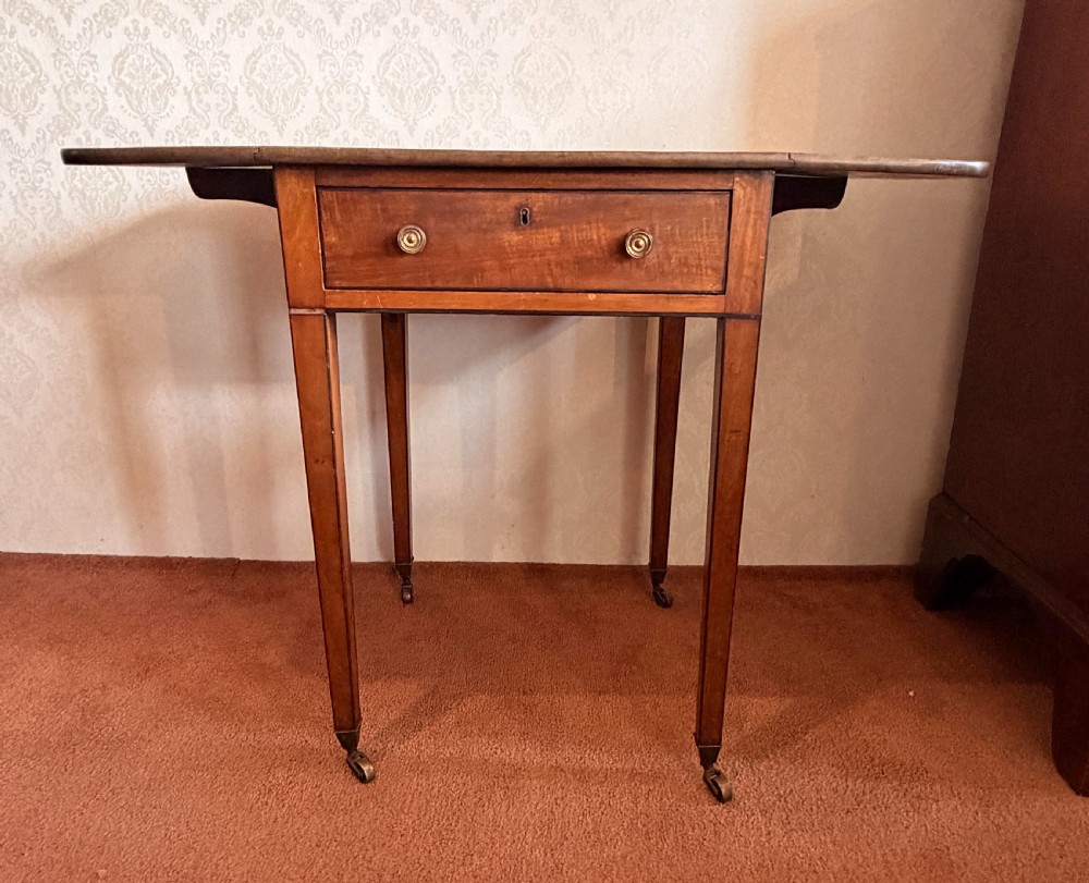A Georgian mahogany Pembroke side table featuring two hinged drop leaves, a single drawer with brass knobs, string-inlaid square tapered legs, and brass castors. View VI