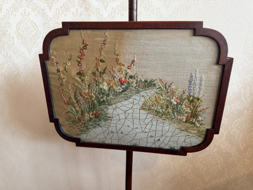A mahogany pole screen featuring a slender turned shaft on a tripod cabriole base with an adjustable framed embroidered panel depicting a garden path. View V