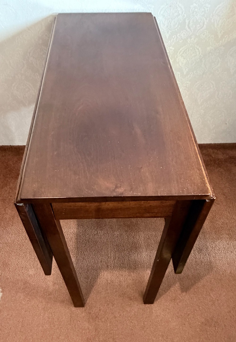 A mahogany drop leaf table shown in the folded position with straight legs and a dark timber finish. View III