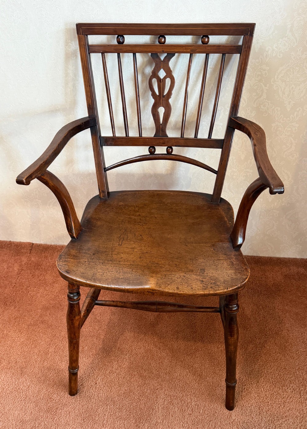 An antique wooden Mendlesham armchair featuring a square back with spindles, spherical bead details, a central pierced splat, curved arms, and a contoured wooden seat.