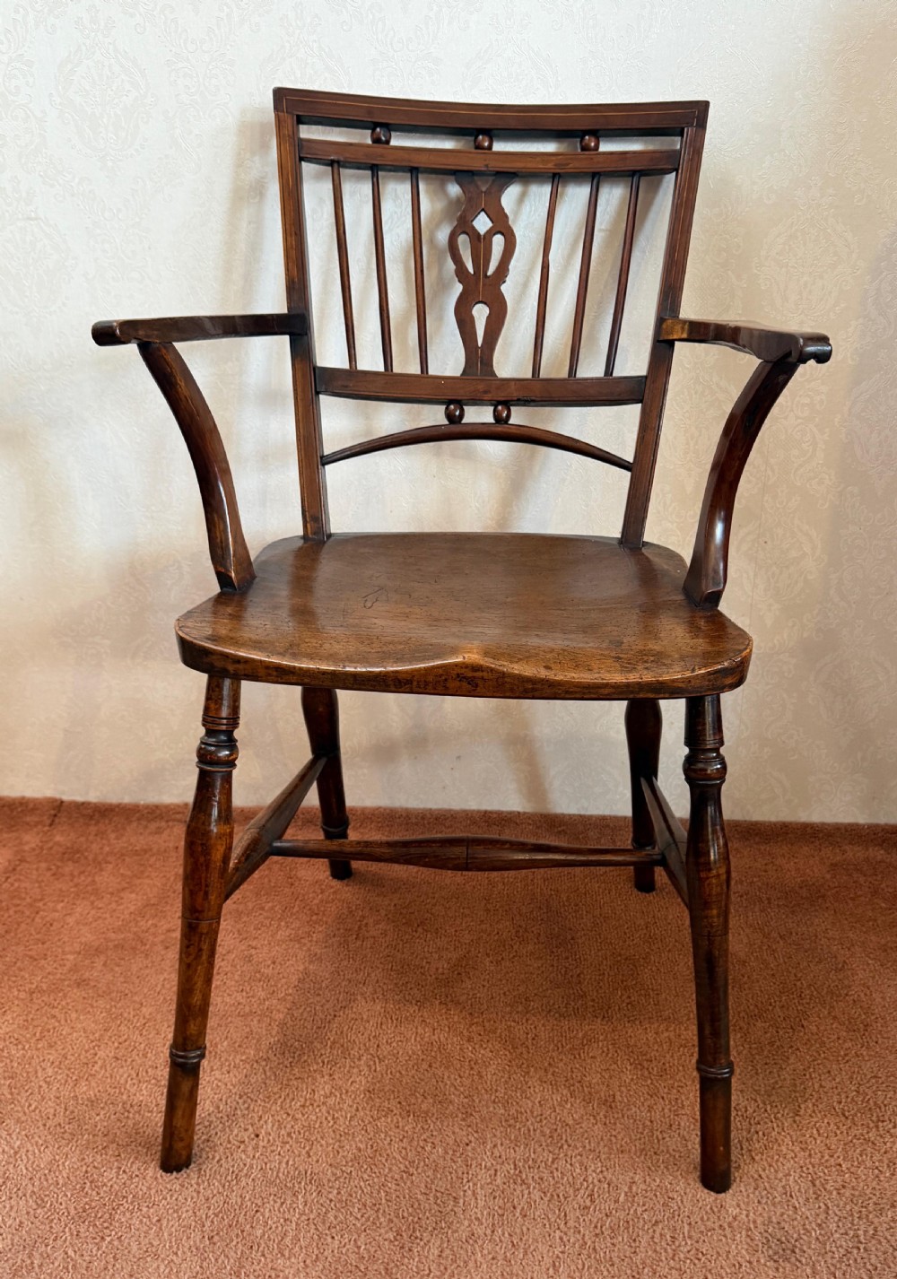 An antique wooden Mendlesham armchair featuring a square back with spindles, spherical bead details, a central pierced splat, curved arms, and a contoured wooden seat. View II