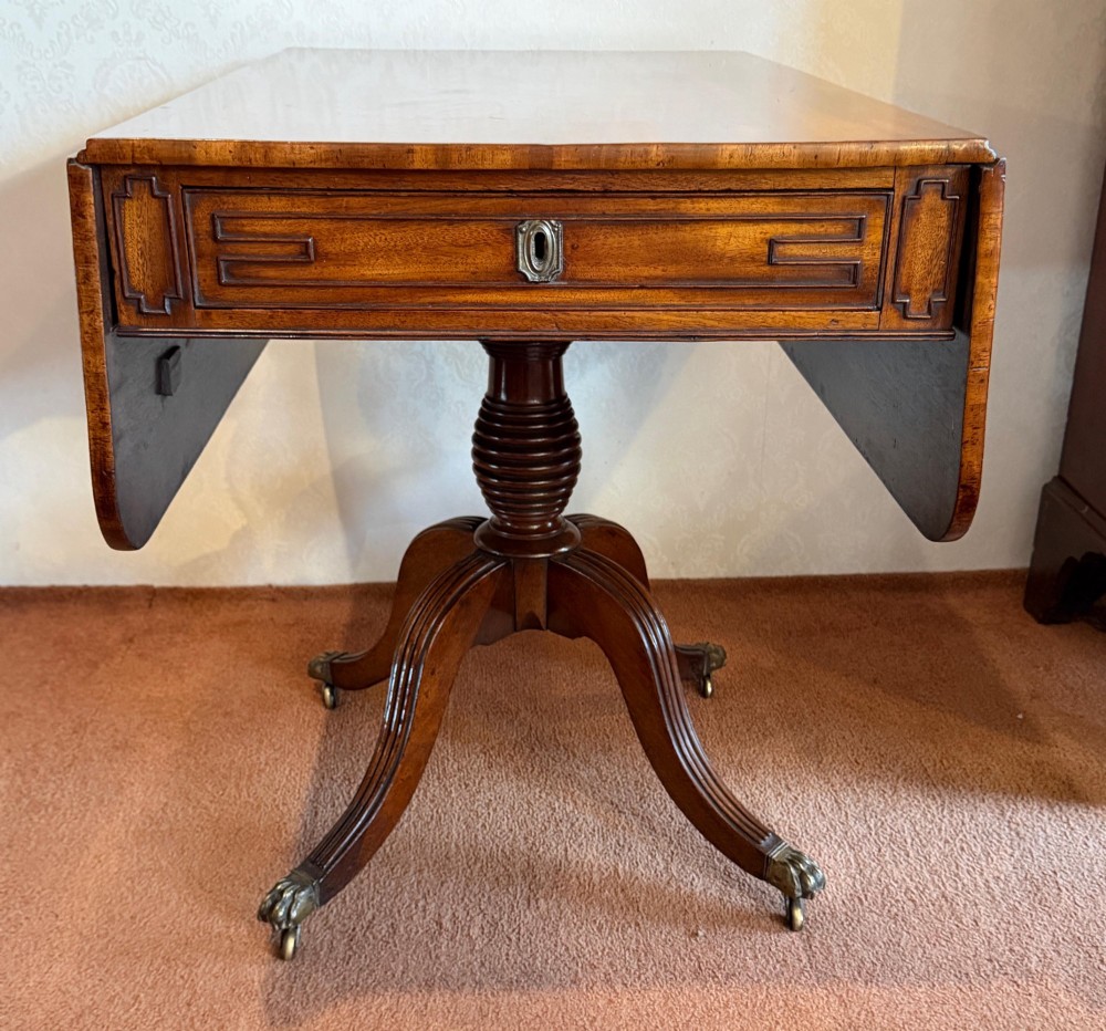 A Regency mahogany drop leaf breakfast table with a reeded central pedestal support and four splayed sabre legs with brass paw castors.