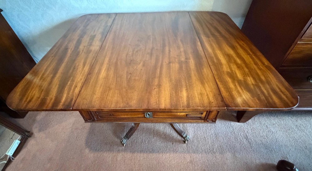 A Regency mahogany drop leaf breakfast table with a reeded central pedestal support and four splayed sabre legs with brass paw castors. View V