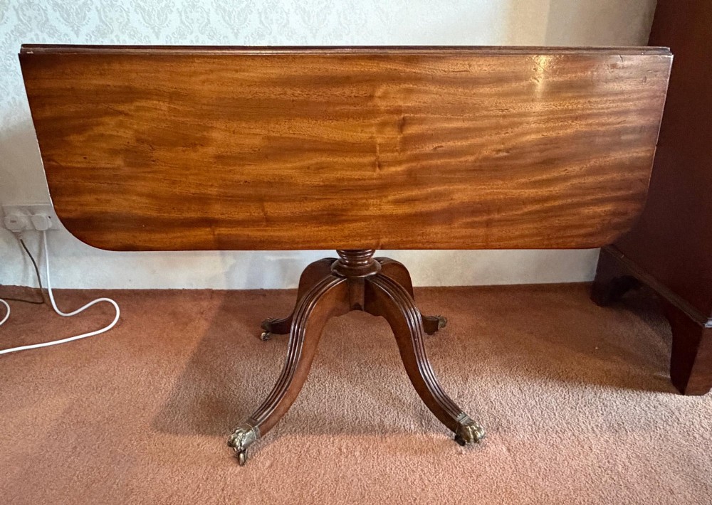 A Regency mahogany drop leaf breakfast table with a reeded central pedestal support and four splayed sabre legs with brass paw castors. View VI