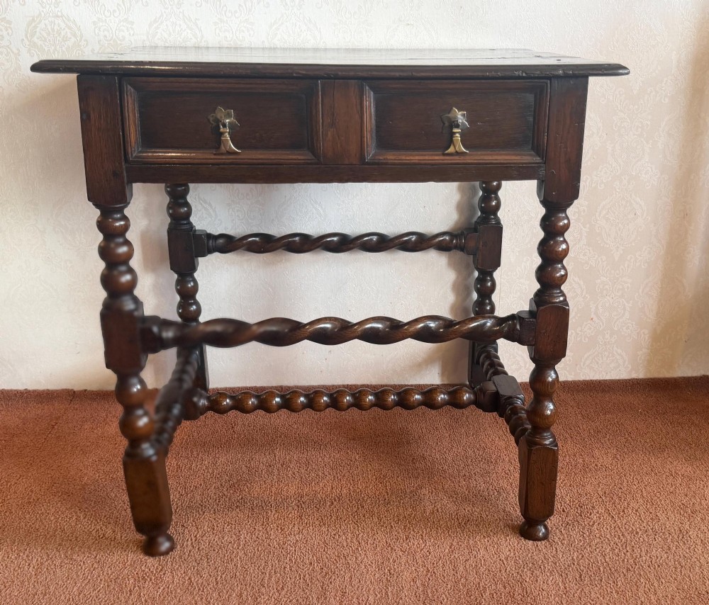 A dark oak side table featuring bobbin-turned legs, barley twist stretchers, and two drawers with brass handles.