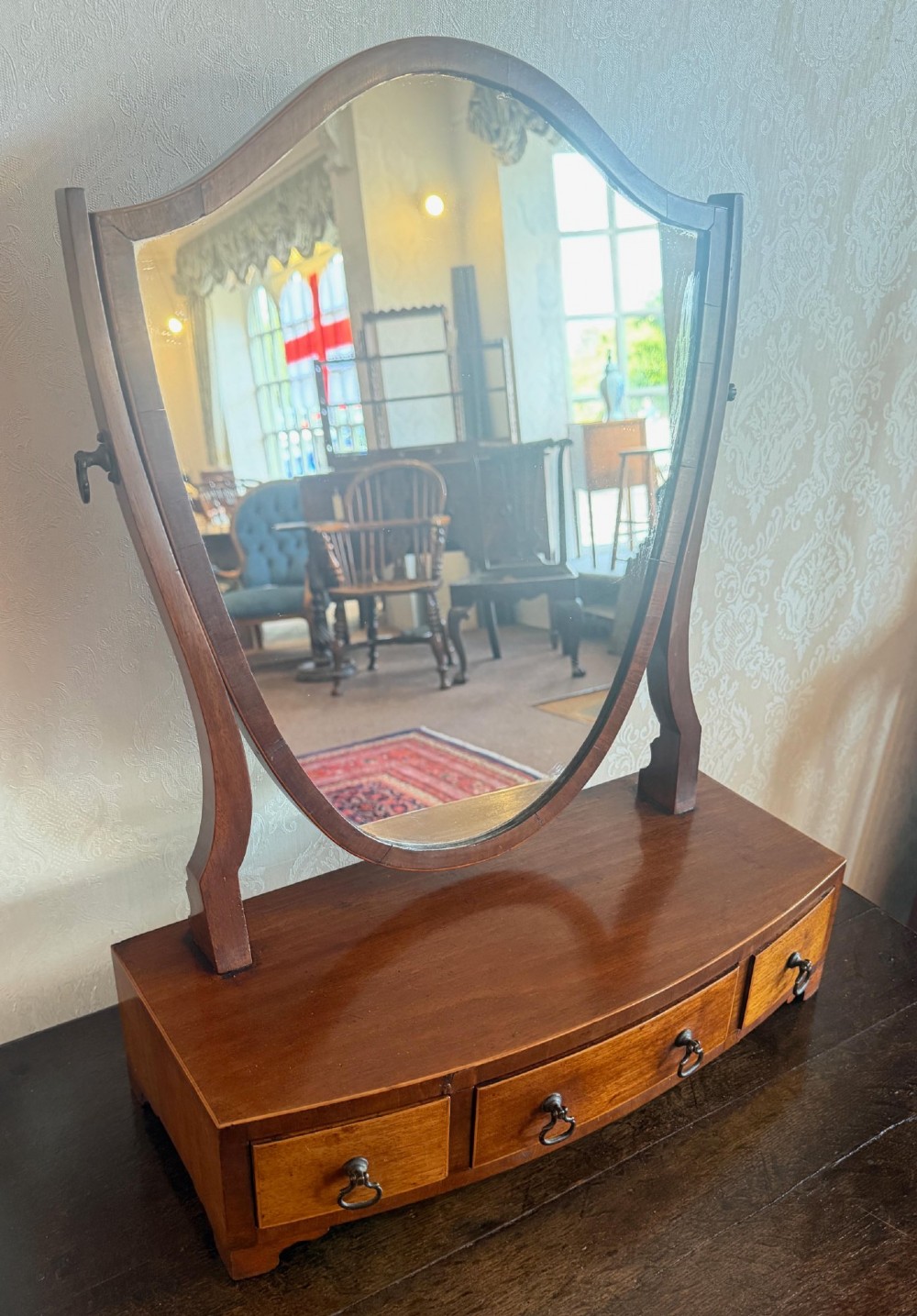 A Georgian style mahogany toilet mirror with a shield-shaped swivel frame set above a bow-fronted base containing three small drawers with brass handles.