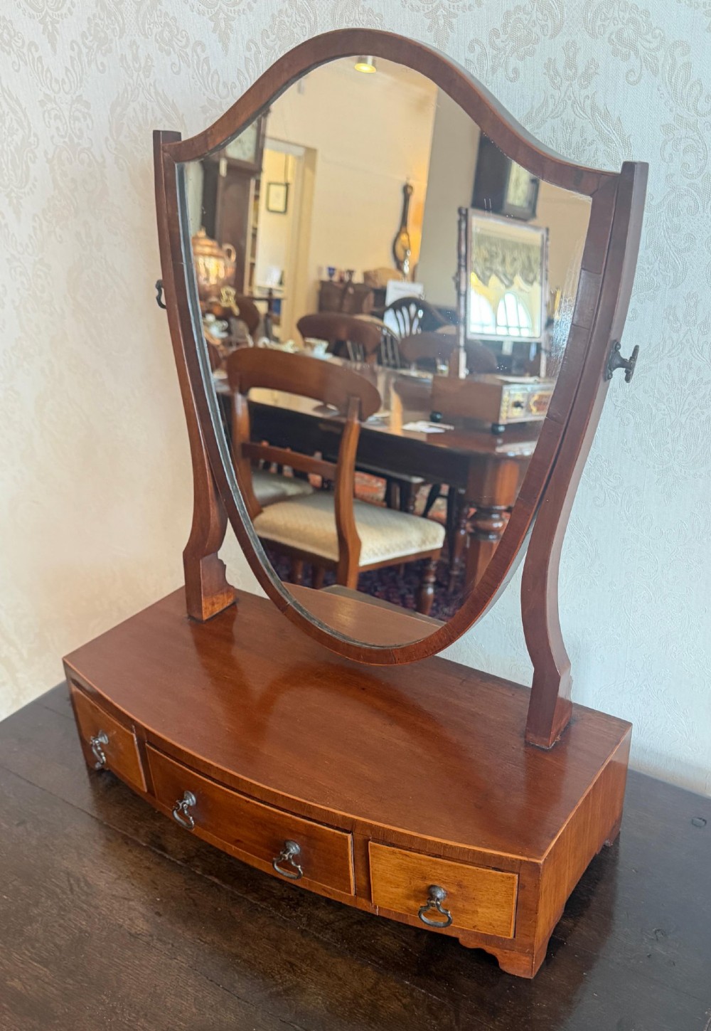 A Georgian style mahogany toilet mirror with a shield-shaped swivel frame set above a bow-fronted base containing three small drawers with brass handles. View II