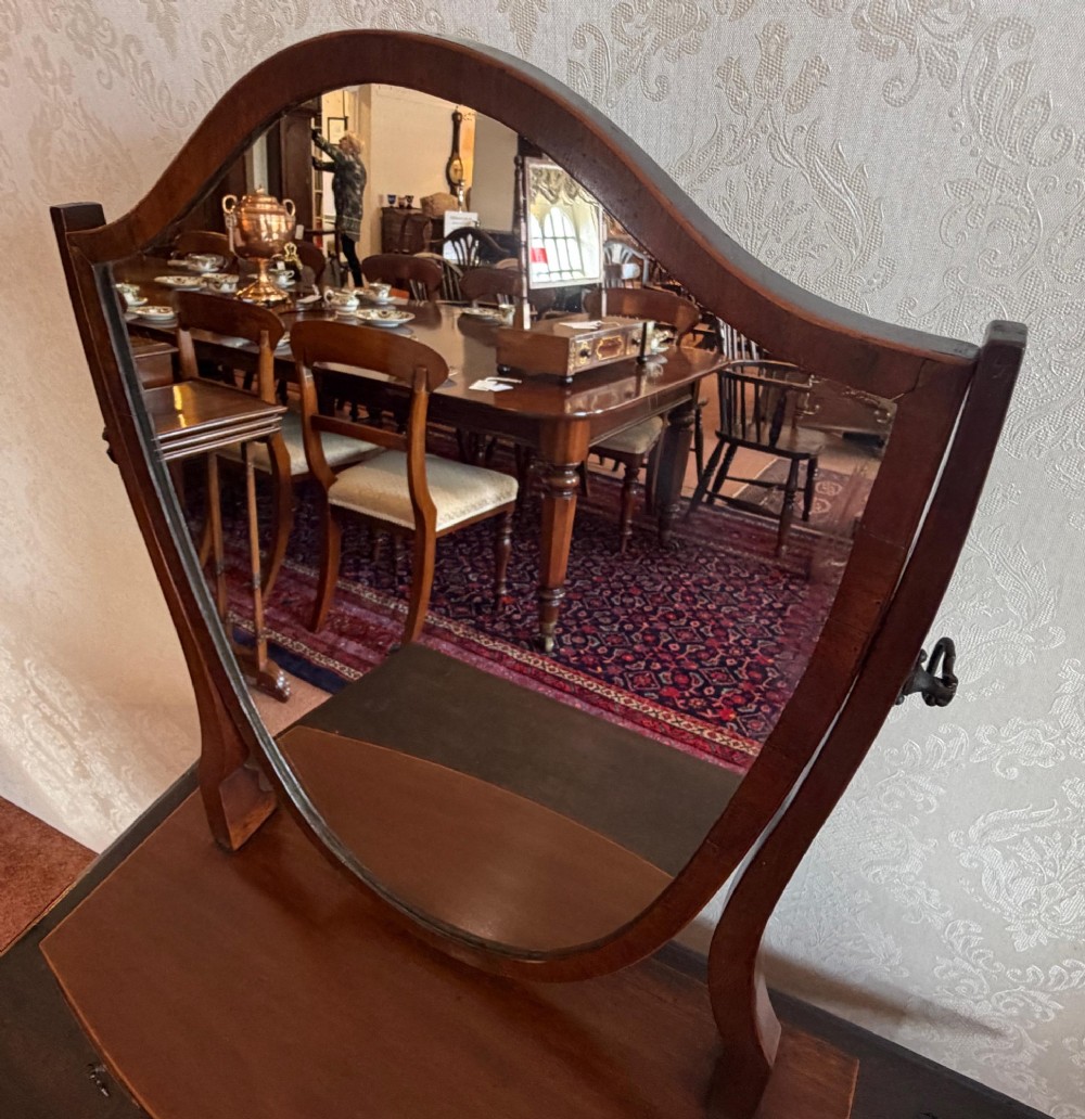 A Georgian style mahogany toilet mirror with a shield-shaped swivel frame set above a bow-fronted base containing three small drawers with brass handles. View VI
