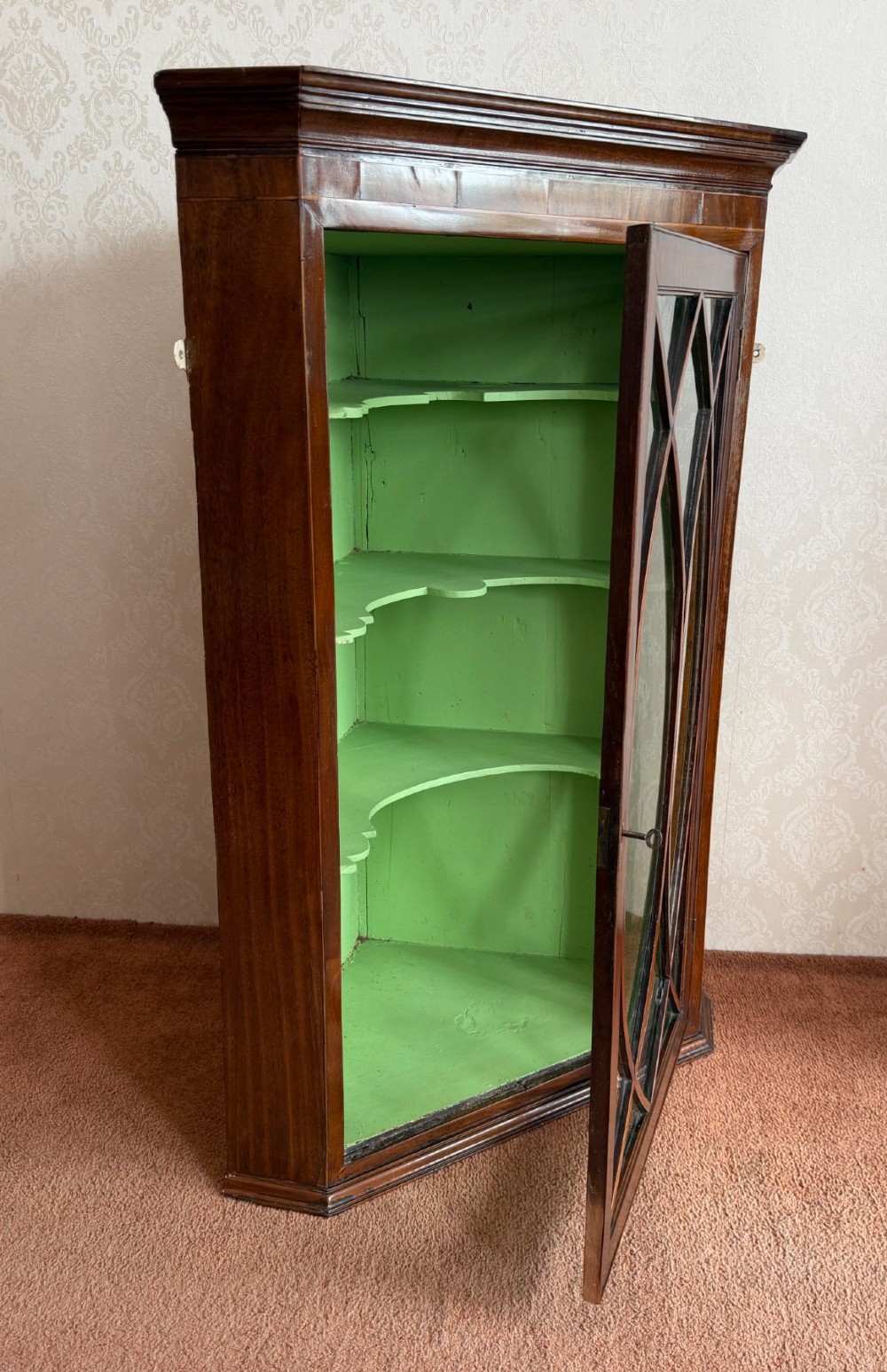 A mahogany wall-hanging corner cupboard featuring an astragal glazed door with oval tracery opening to reveal green shelves. View V