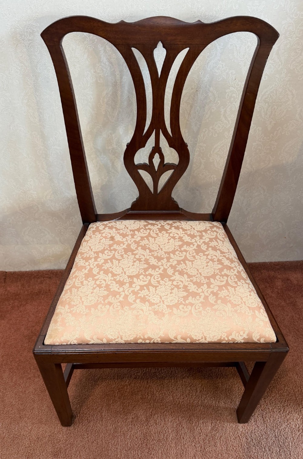 A mid-18th-century mahogany dining chair featuring a carved pierced back splat, serpentine crest rail, and a patterned damask drop-in seat.